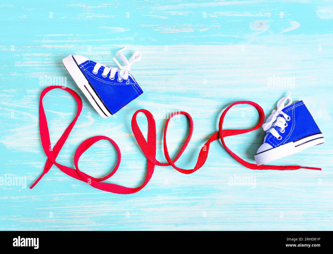 Chaussures miniatures en toile bleue pour les tout-petits et mot AMOUR fait à partir d'un lacet rouge sur un fond en bois bleu. Concept lié à la mode pour enfants. Banque D'Images