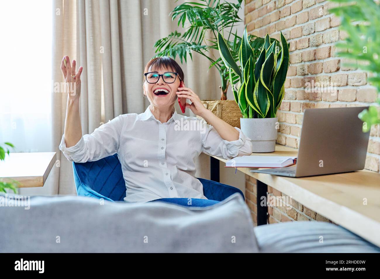 Heureuse femme d'âge moyen parlant sur le téléphone portable, à la maison Banque D'Images