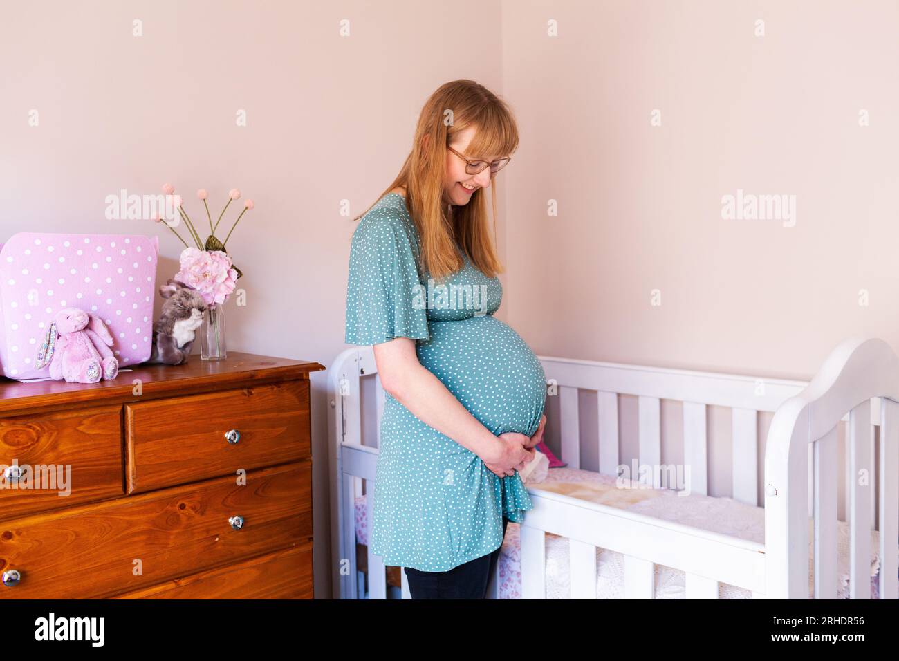 Jeune femme enceinte dans la vingtaine debout près d'un lit dans la crèche Banque D'Images