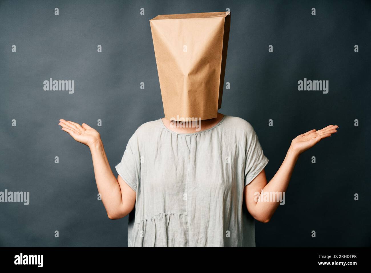 Femme confuse avec sac en papier au-dessus de la tête sur fond sombre. Concept d'émotions Banque D'Images