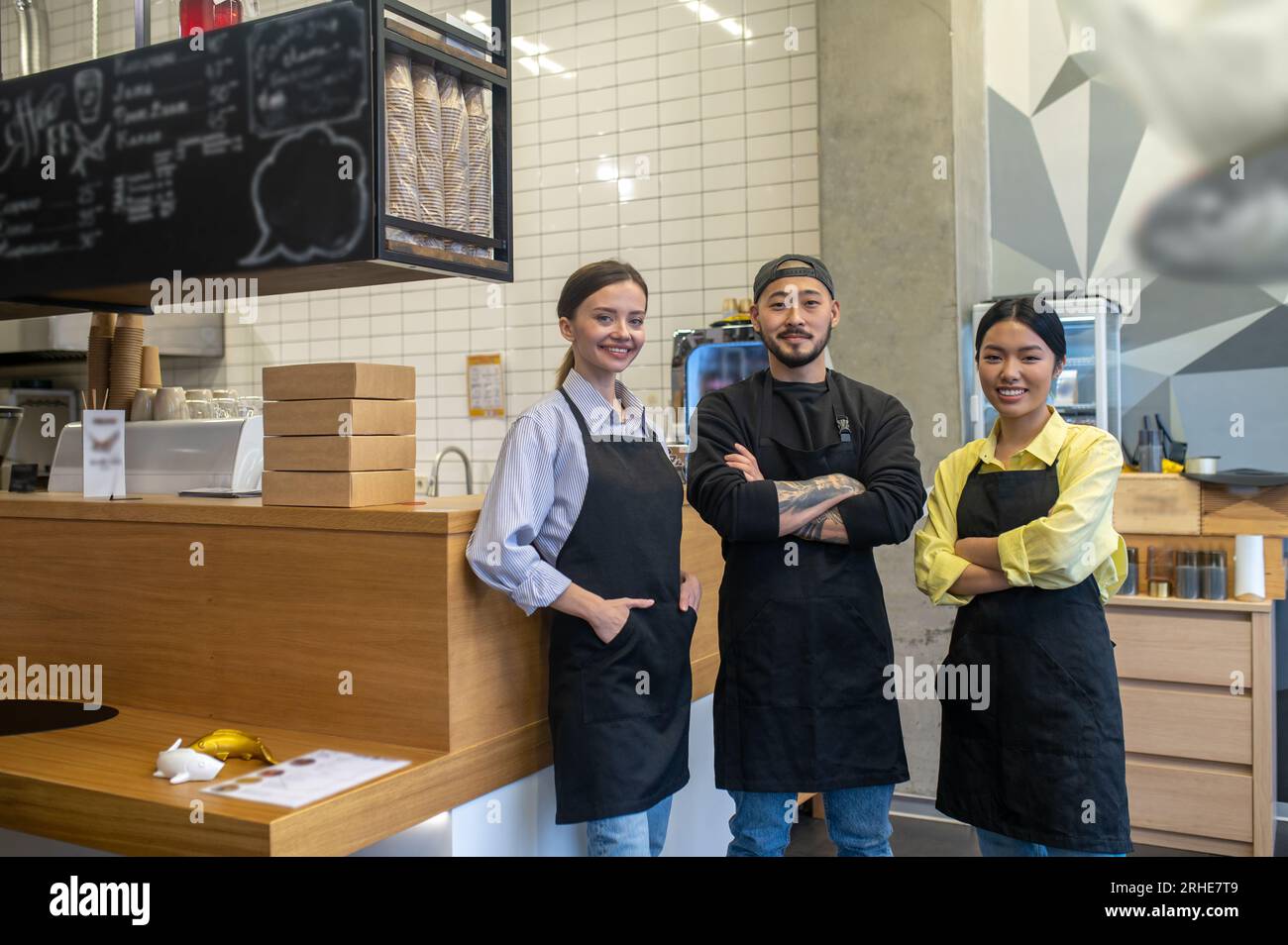 Équipe de jeunes ouvriers de café debout ensemble et l'air satisfaits Banque D'Images