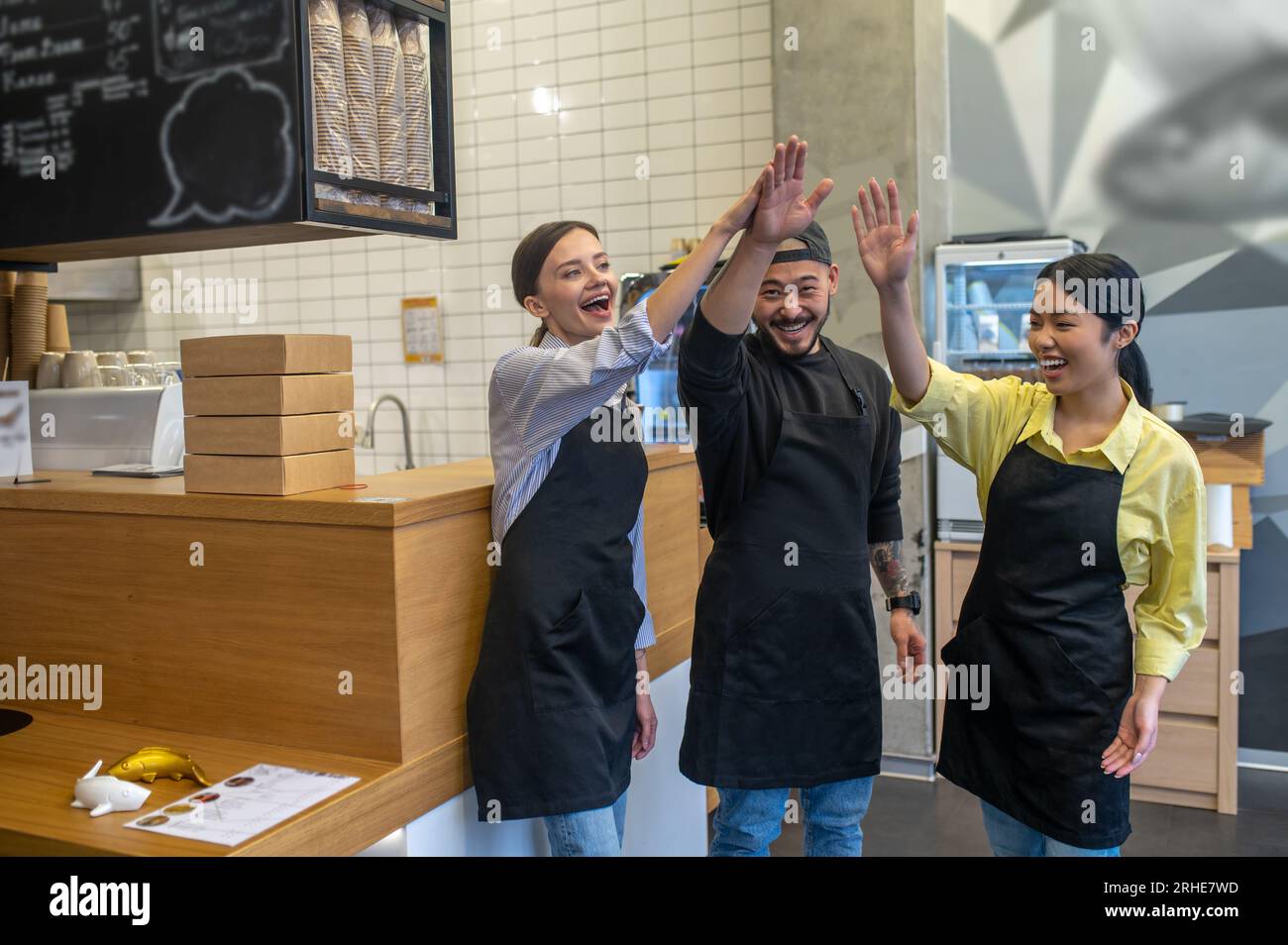 Équipe de jeunes ouvriers de café debout ensemble et l'air satisfaits Banque D'Images