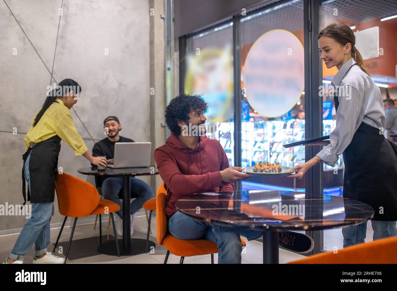 Serveuse souriante passant l'assiette avec des sushis au client au café Banque D'Images