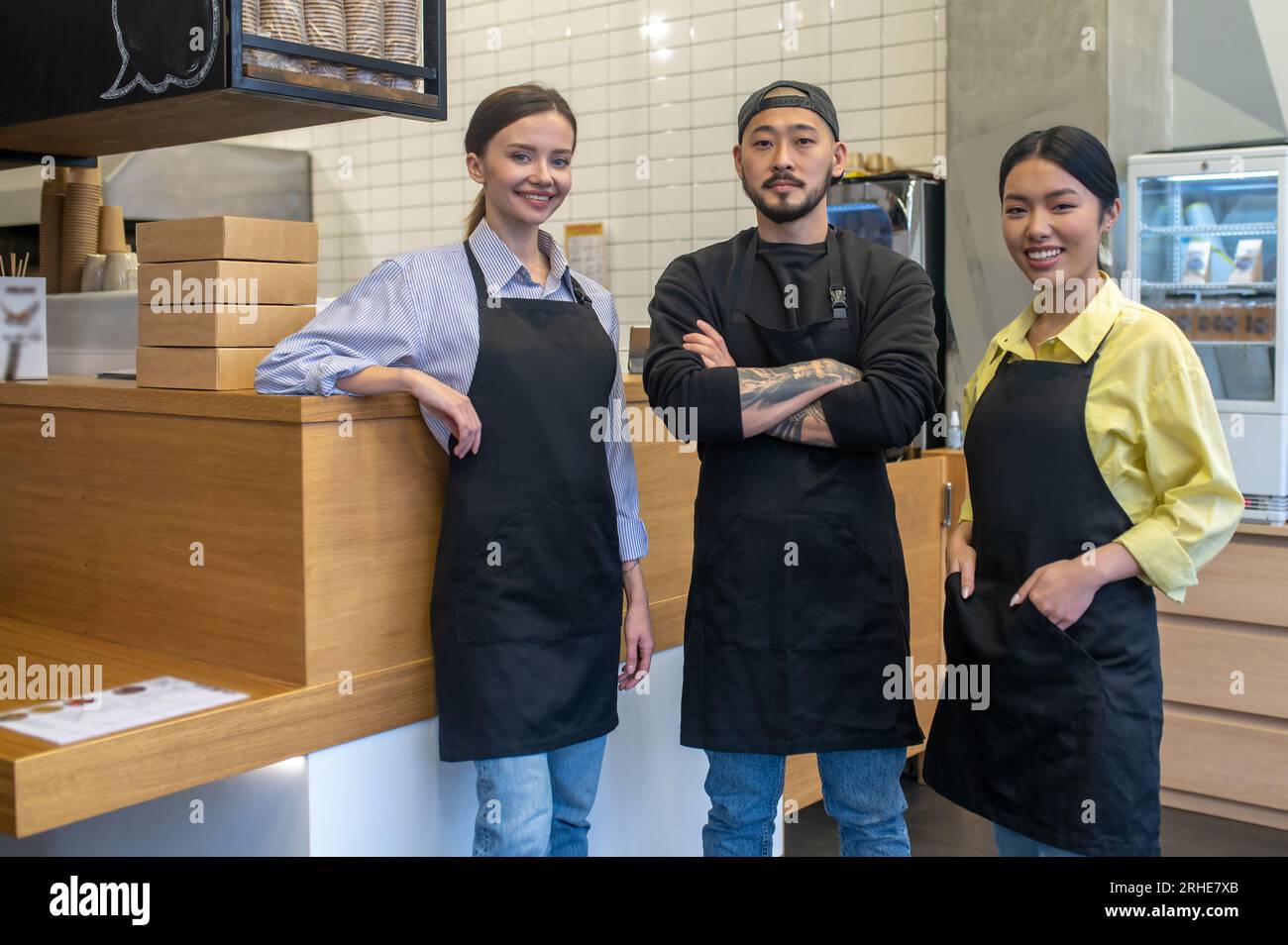 Équipe de jeunes ouvriers de café debout ensemble et l'air satisfaits Banque D'Images