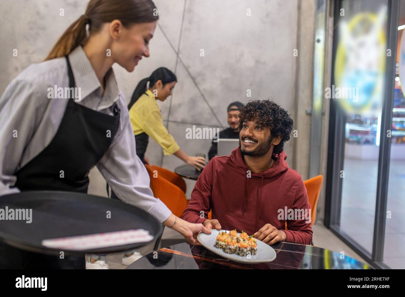 Serveuse souriante passant l'assiette avec des sushis au client au café Banque D'Images