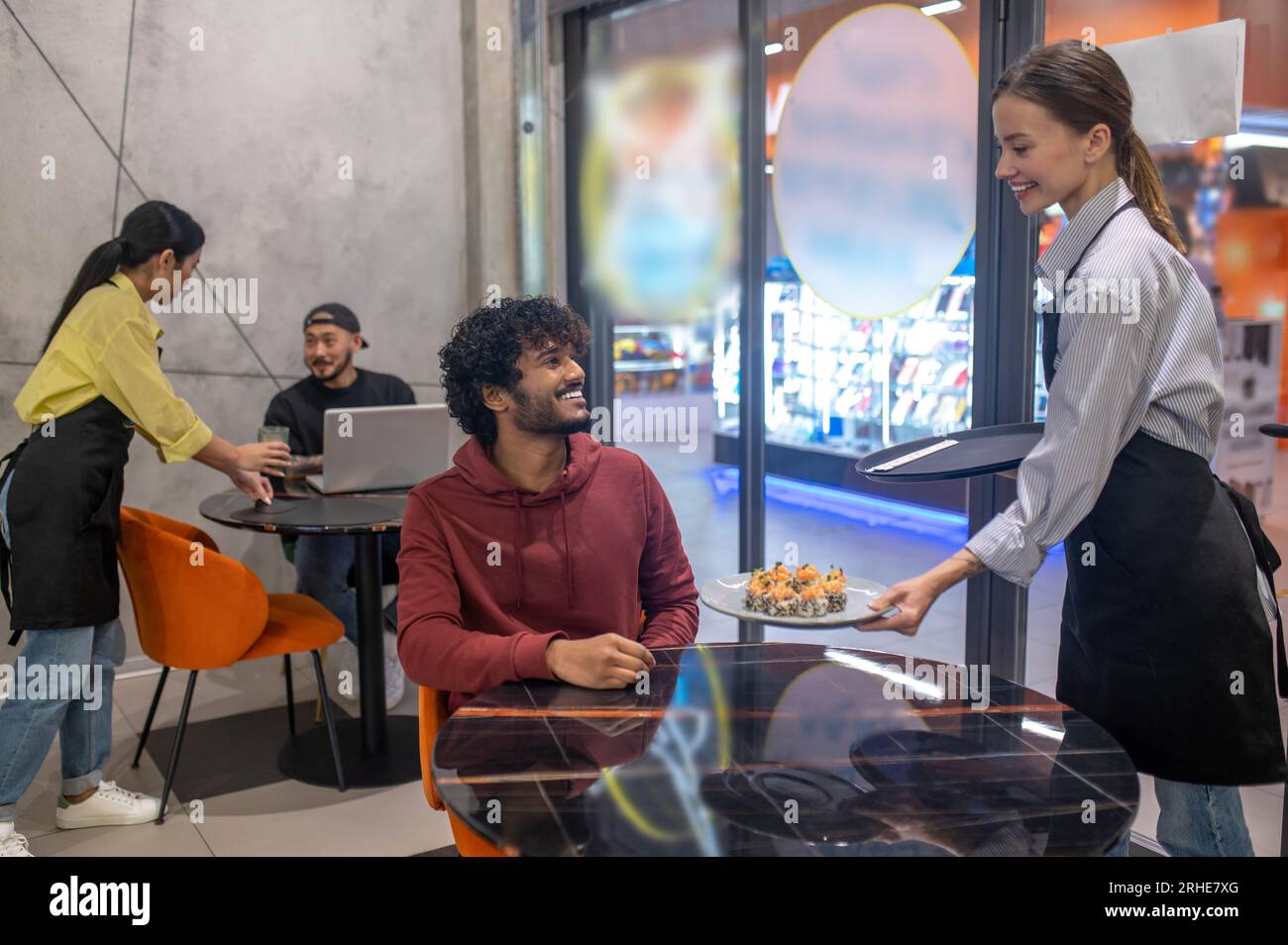 Serveuse souriante passant l'assiette avec des sushis au client au café Banque D'Images