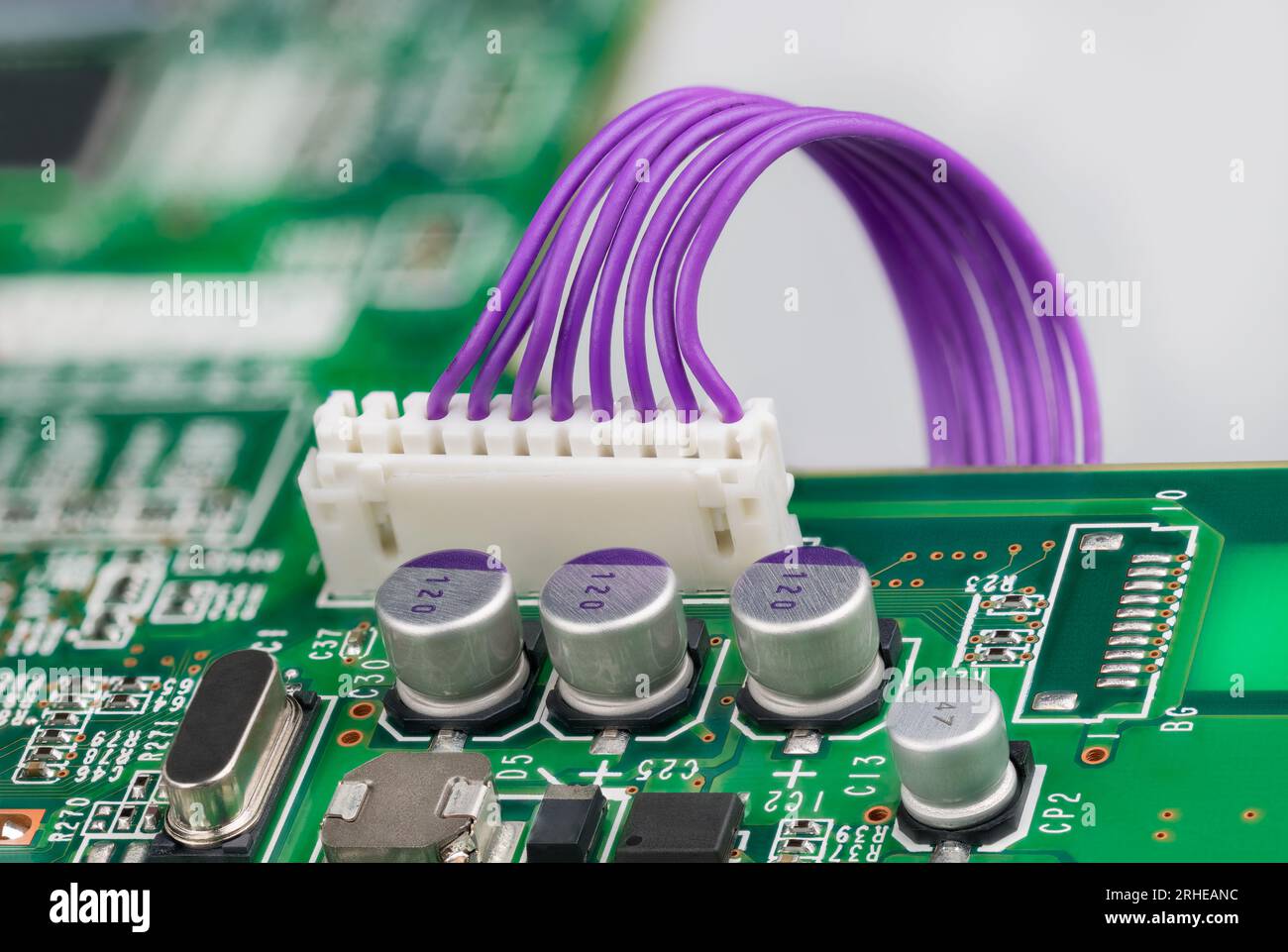 Condensateurs électrolytiques et connecteur en plastique blanc avec câbles violets, cristal ou diode sur carte verte. Circuit imprimé et composants électroniques. Banque D'Images
