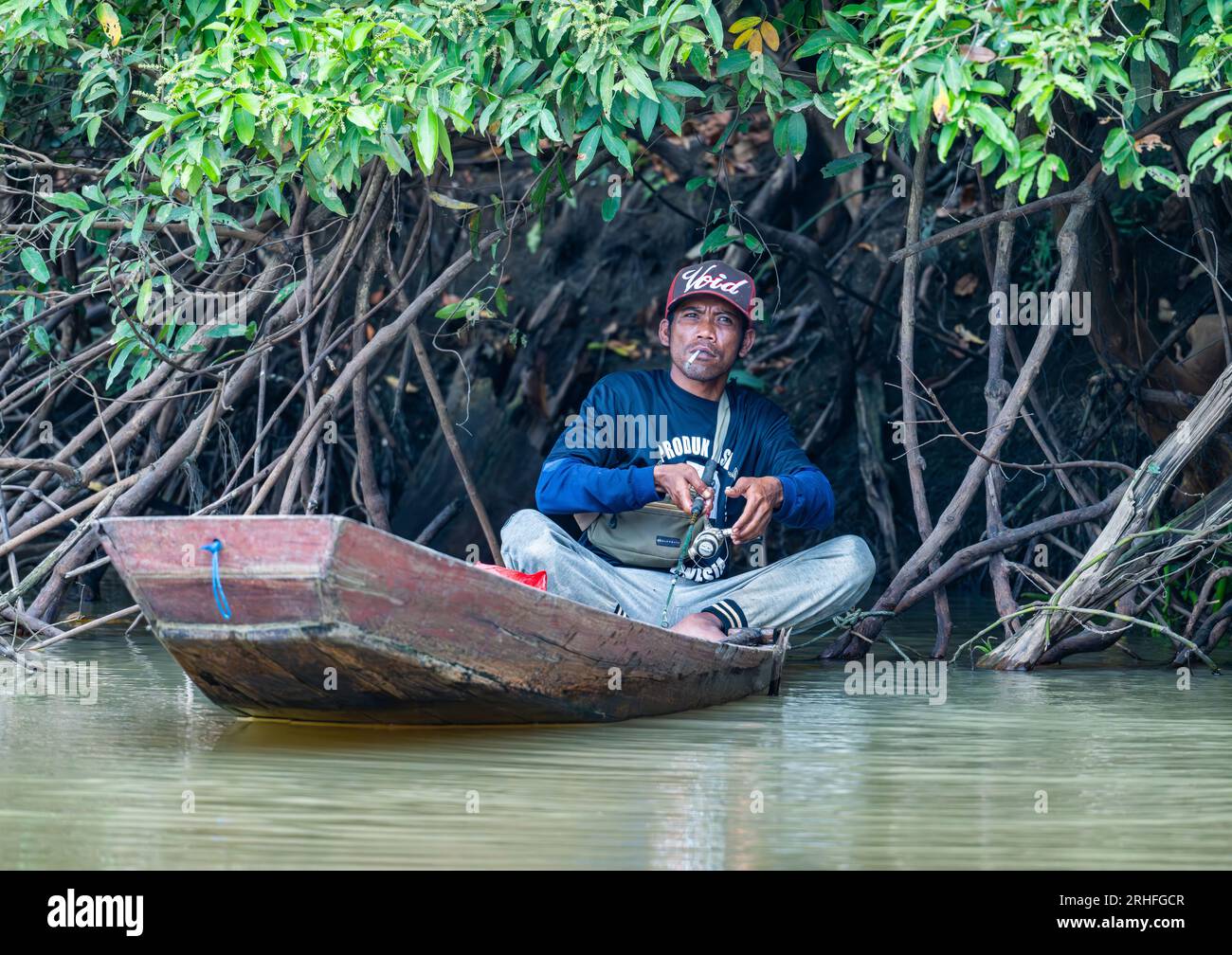 Un homme fumant et pêchant à partir d'un petit bateau sur une rivière. Sumatra, Indonésie. Banque D'Images Un homme fumant et pêchant à partir d'un petit bateau sur une rivière. Sumatra, Indonésie. Banque D'Images