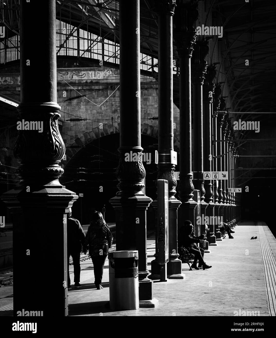 L'image monochromatique révèle une scène de gare avec une colonnade proéminente s'étendant sur le fond, flanquée de colonnes. Banque D'Images