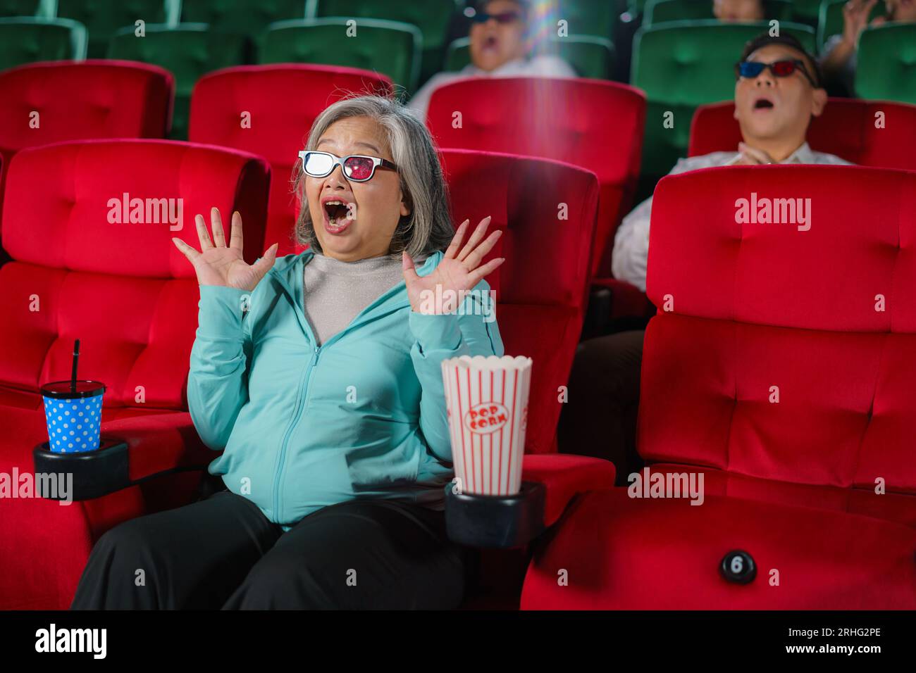 Les femmes âgées asiatiques avec des lunettes regardent avec impatience des films 3D, pop-corn à la main, savourant l'expérience immersive. Banque D'Images