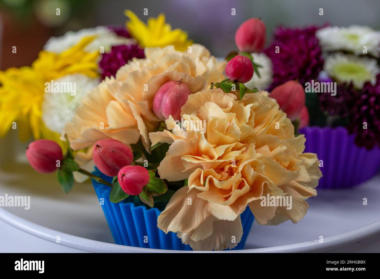 Vue rapprochée d'un bel arrangement floral de fleurs colorées disposées dans des tasses à cupcake cannelées, avec fond défocalisé. Banque D'Images
