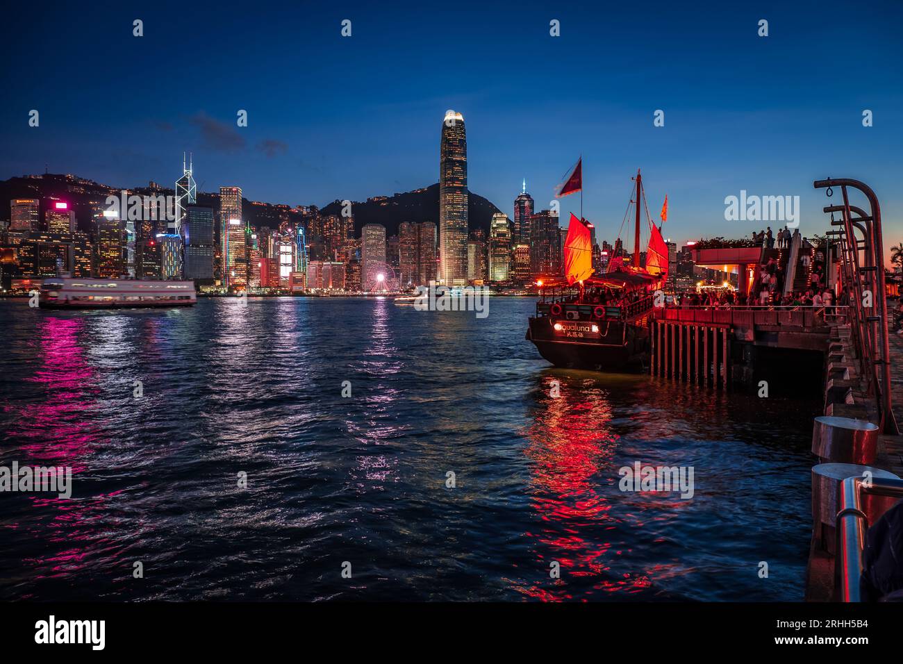 Superbe vue nocturne d'une jonque illuminée dans le port Victoria en face de l'horizon fantastique de Hong Kong avec ses impressionnants gratte-ciel Banque D'Images