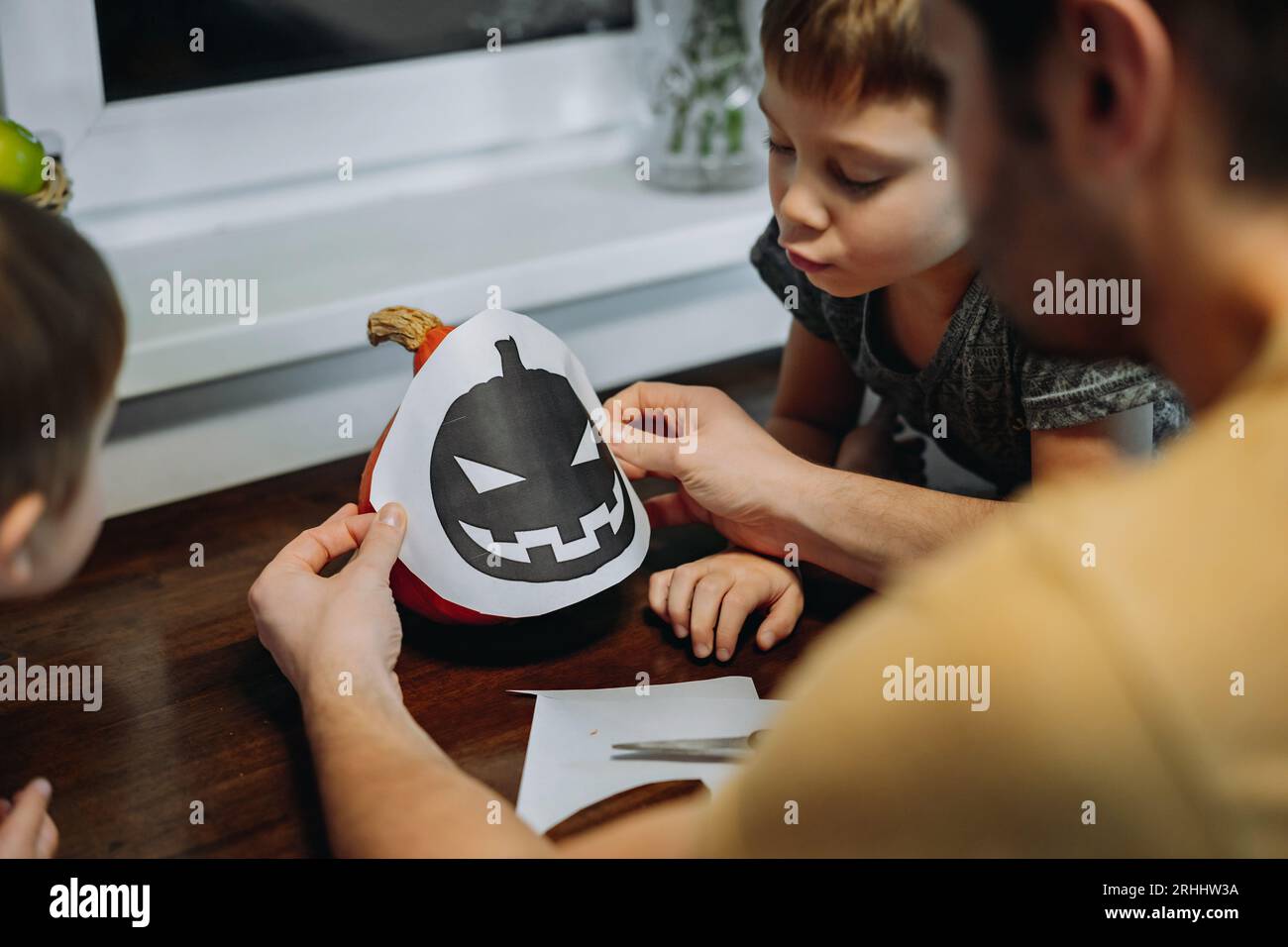 Ather et deux enfants découpent un modèle pour faire Jack Lantern à partir de citrouille orange. Image avec mise au point sélective. Photo de haute qualité Banque D'Images