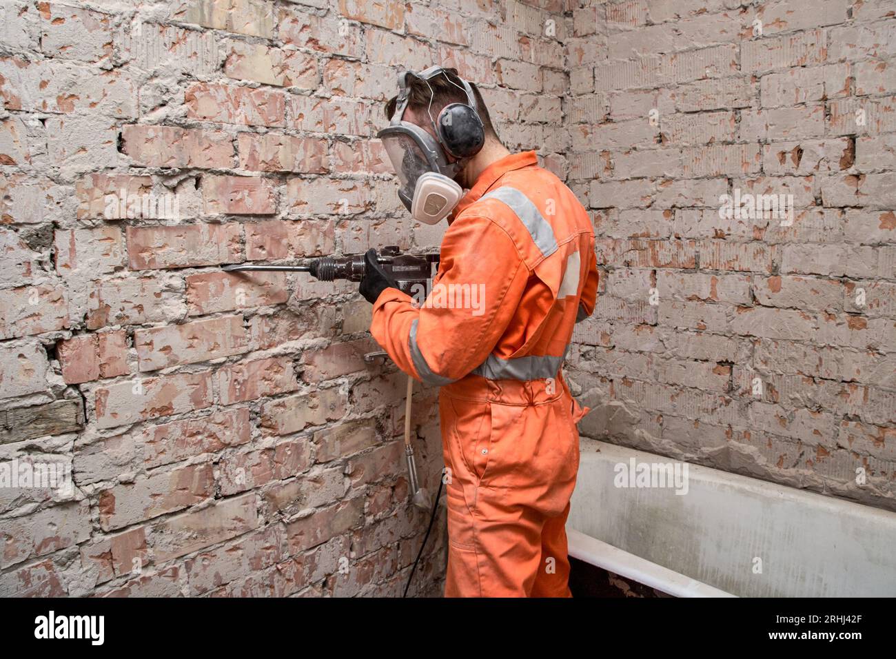 Travailleur masculin portant un masque respiratoire intégral et un casque antibruit pour travailler dans un environnement poussiéreux et bruyant tout en utilisant une perceuse à percussion. Banque D'Images