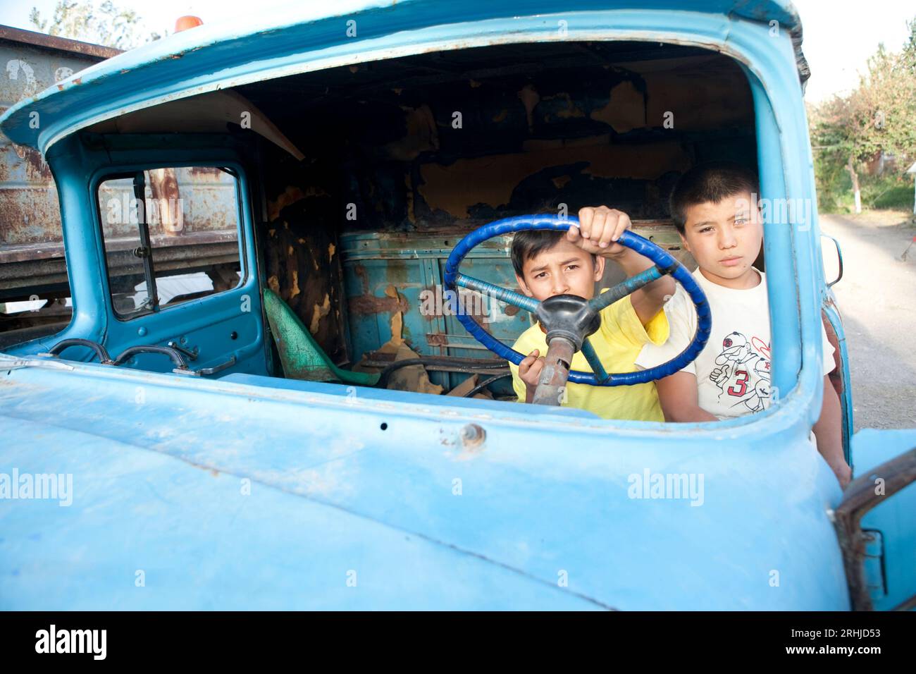 Des enfants jouent dans la coquille rouillée d'un vieux camion soviétique à l'intérieur d'un camp pour personnes déplacées (PDI) dans le quartier Sharq d'Osh, au Kirghizistan Banque D'Images