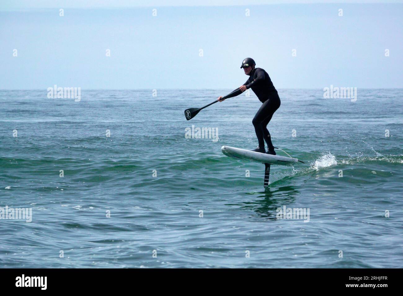 Un homme en combinaison monte une vague sur une planche de surf hydroptère, également appelée foil de levage, sur la côte Pacifique de l'Oregon. Banque D'Images