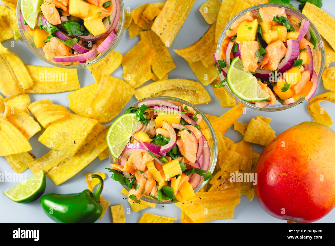 Plats de Ceviche de saumon avec mangue entouré de croustilles plantains : bols de ceviche de saumon avec des croustilles plantains et des ingrédients sur fond bleu Banque D'Images