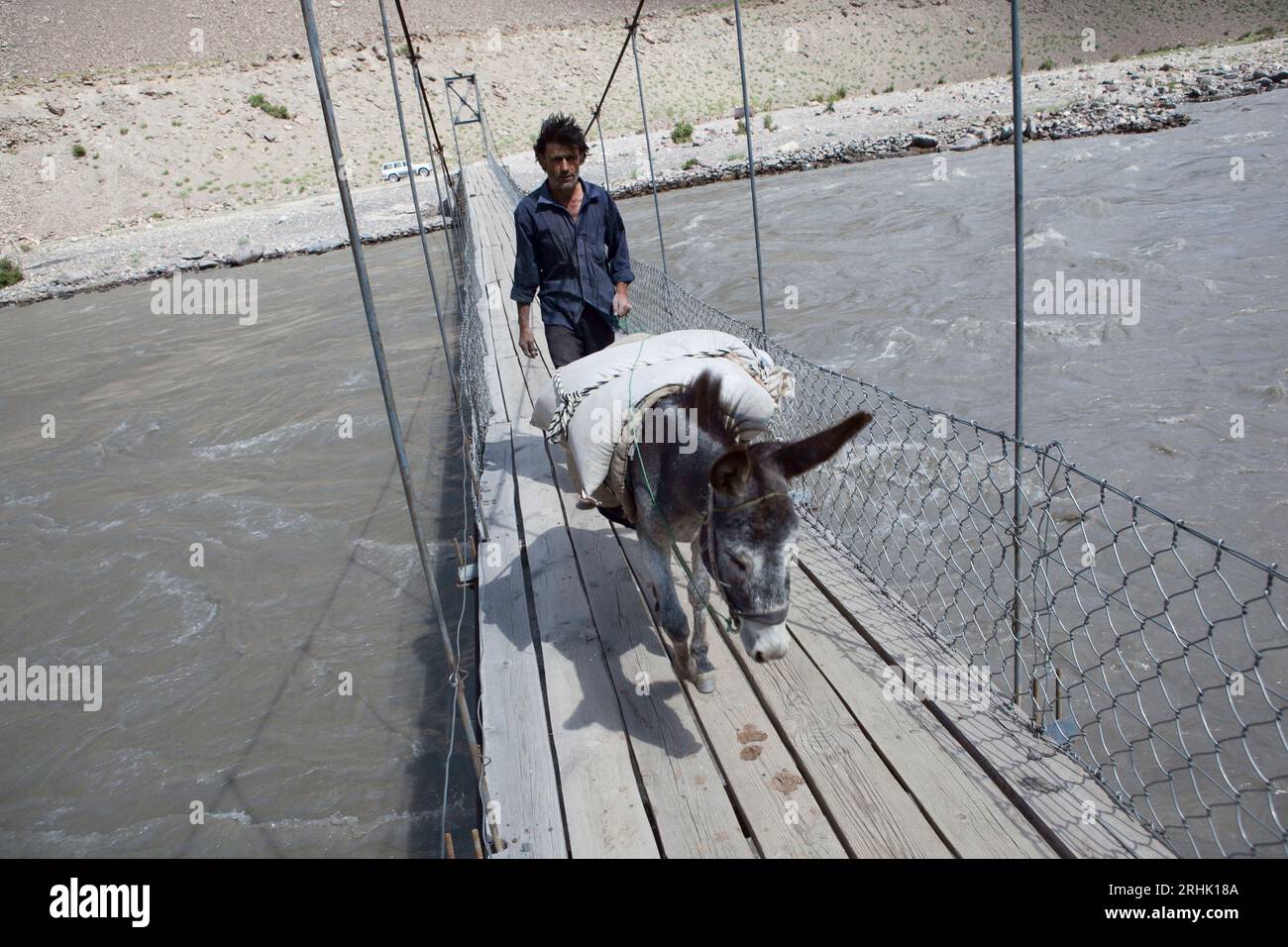 Un homme avec un âne chargé traverse un pont près de Basid, vallée de Bartang, Tadjikistan. Banque D'Images