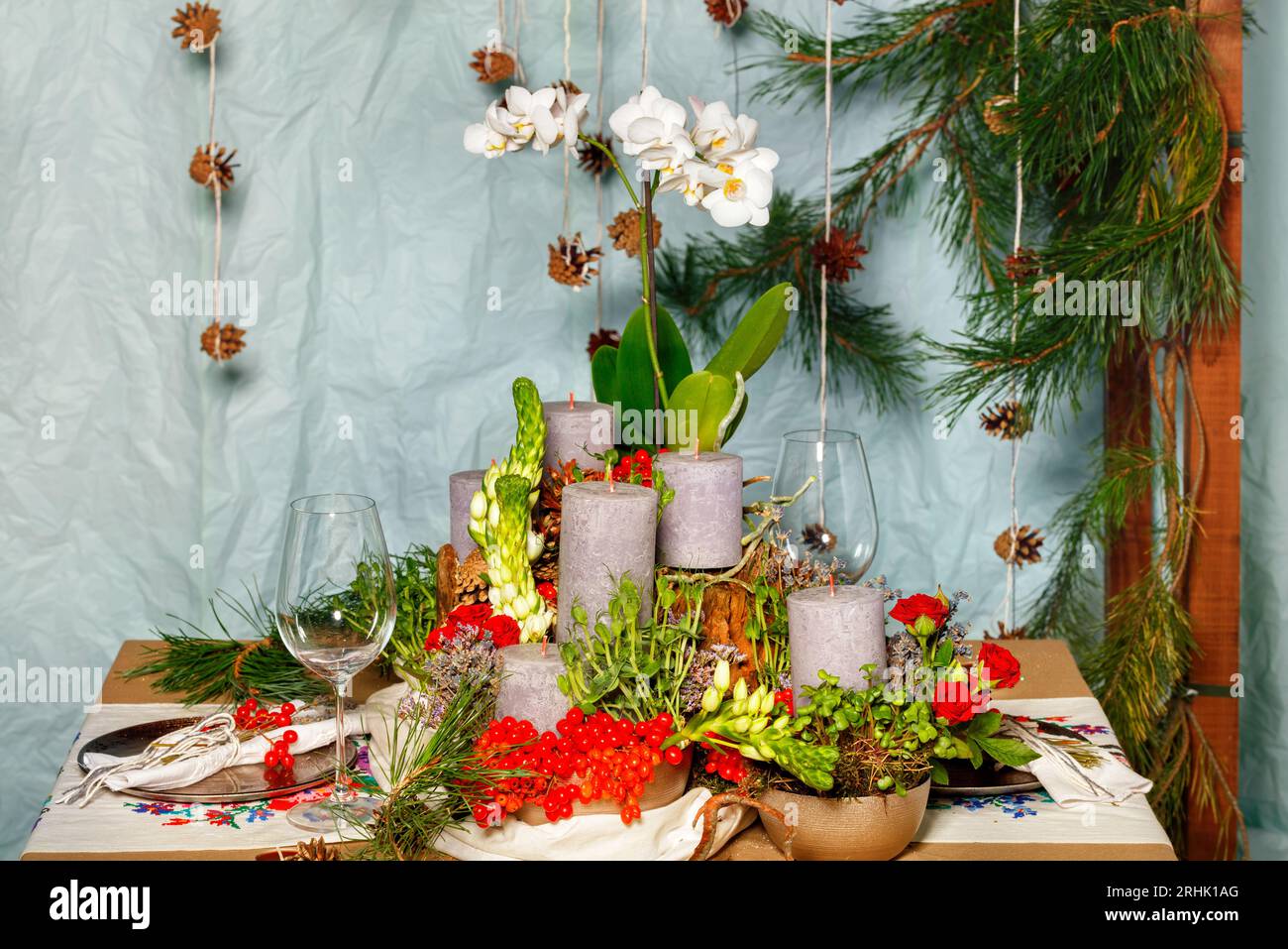 Nature morte du nouvel an, bougies épaisses parmi les baies de viburnum, branches d'épinette, fleurs blanches d'orchidée et gobelets en verre. Banque D'Images