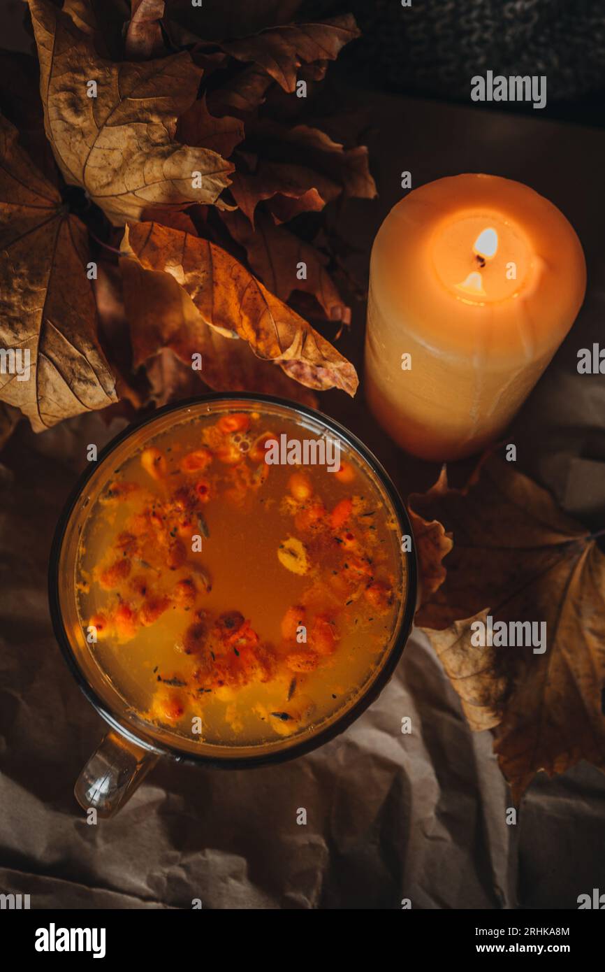 Bougie brûlante et une grande tasse de thé d'argousier orange chaud dans une maison confortable soirée d'automne encore la vie avec des feuilles sèches. Banque D'Images