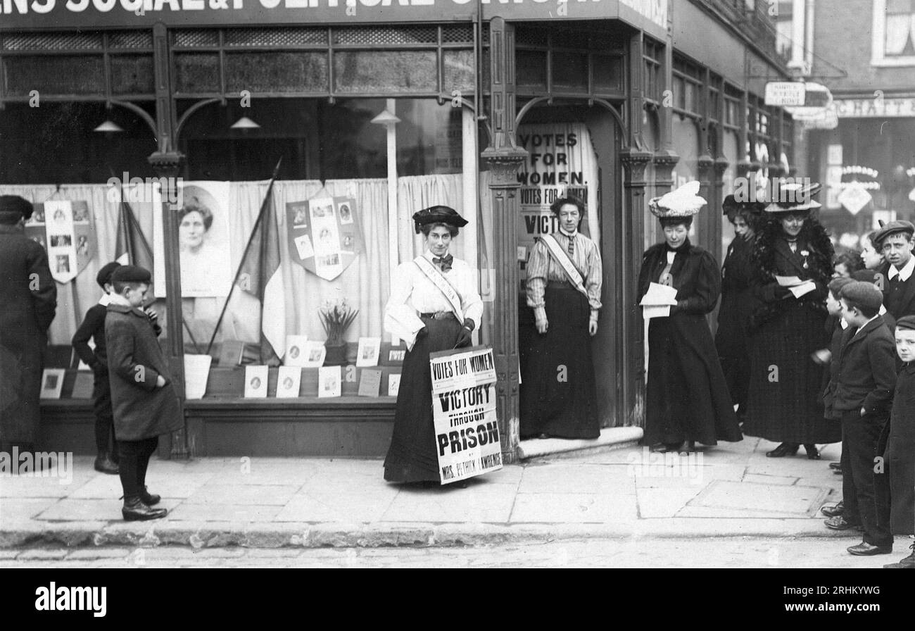 Kensington Women's social & Political Union, Mary Sinclair debout à l'extérieur de la boutique avec l'affiche « Victory Through prison » avec des enfants et d'autres suffragettes, des dépliants, des drapeaux et une image d'Emmeline Pankhurst dans la vitrine Banque D'Images