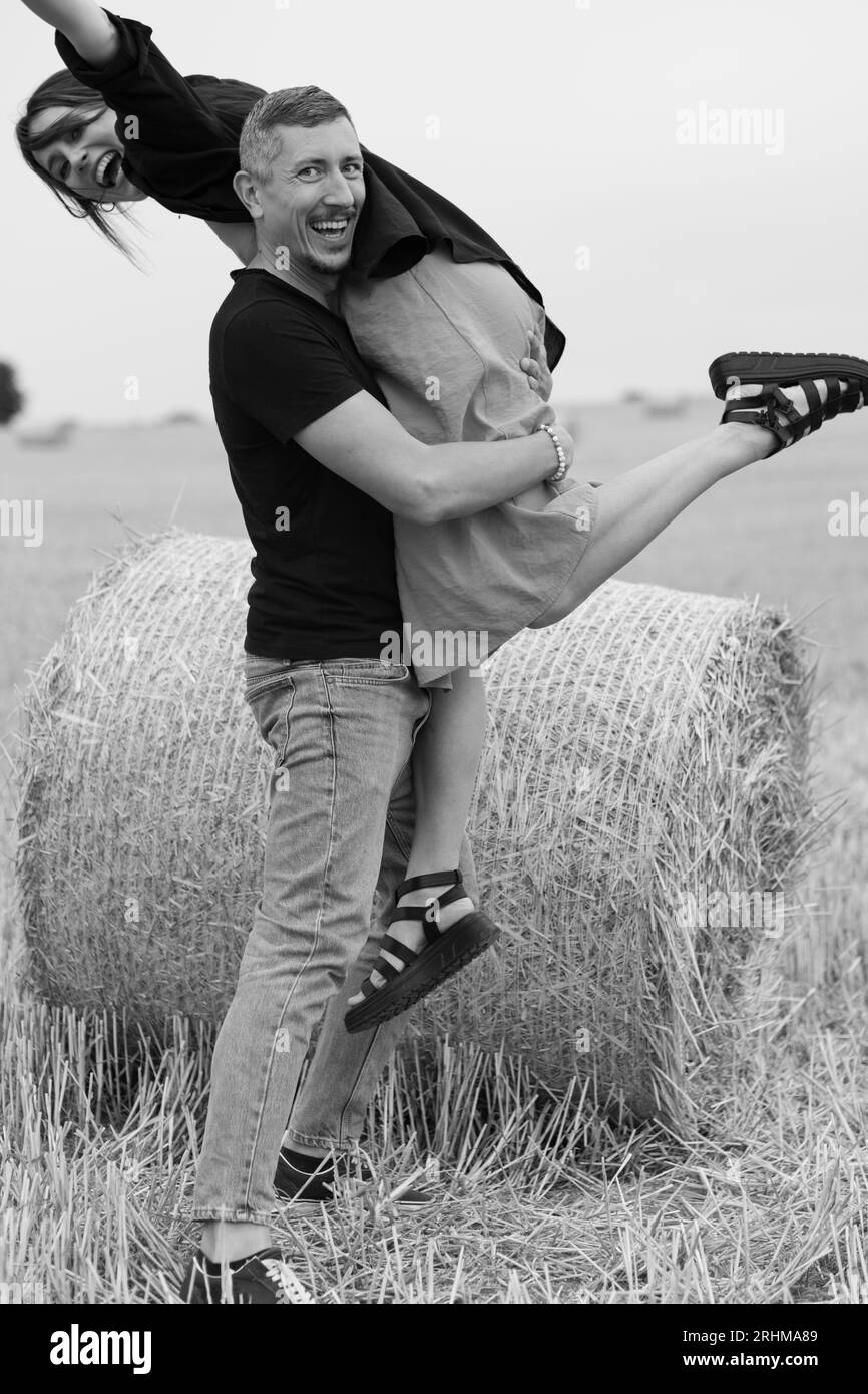 Un jeune couple de belles personnes s'amusent dans le champ près des balles rondes de foin sec. Un homme dansant avec sa femme près d'une balle de paille. Noir et blanc Banque D'Images