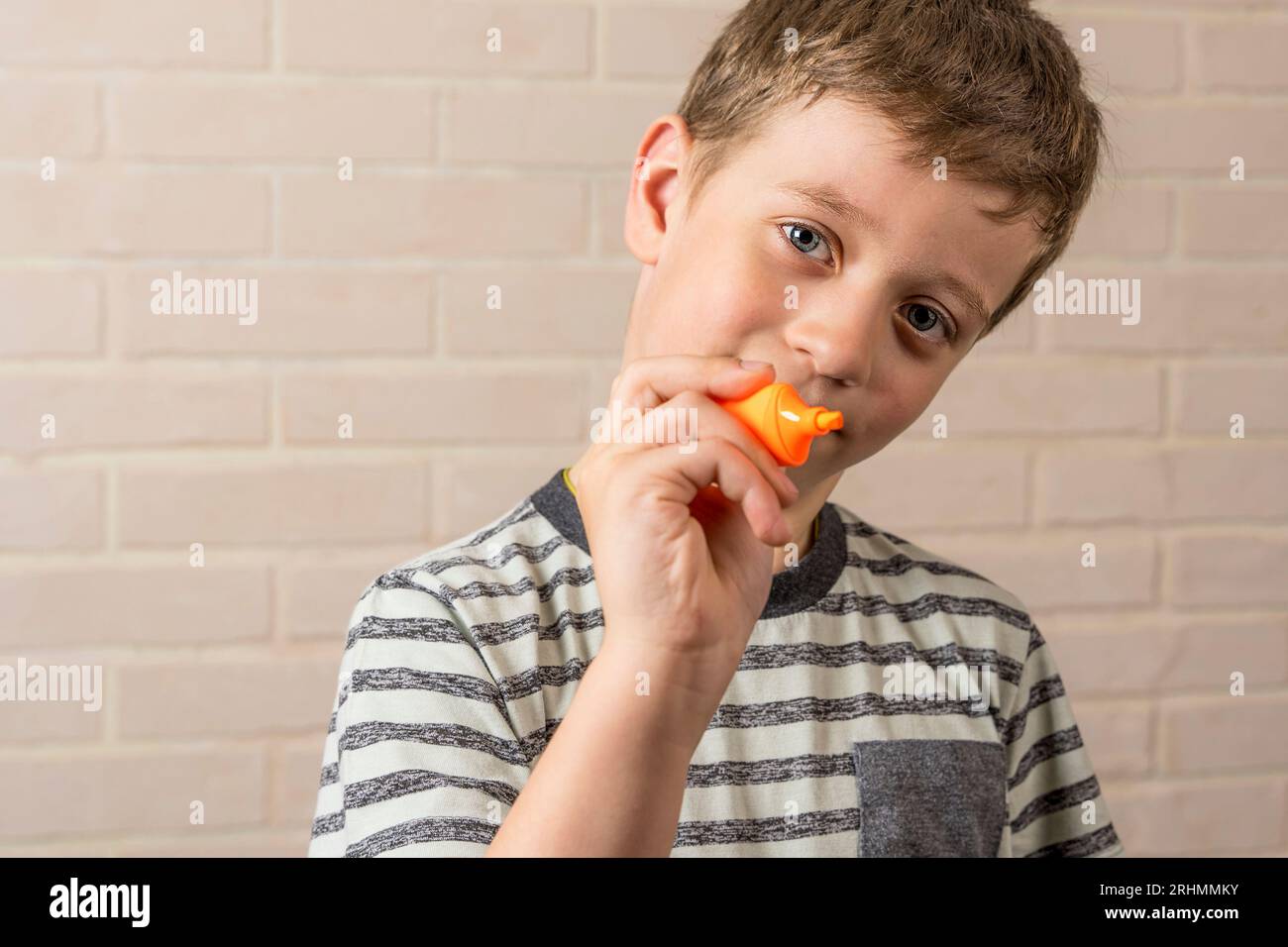 un garçon d'âge scolaire écrit des mots invisibles en l'air avec un marqueur orange. Le concept d'études, d'activités scolaires et d'éducation Banque D'Images