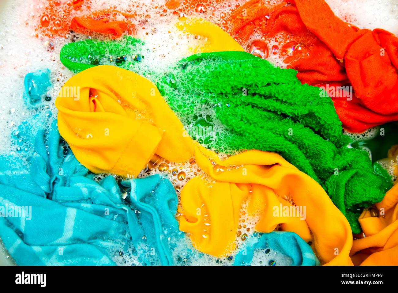 Vêtements colorés trempés dans de l'eau avec du détergent et des bulles de mousse. Lavage à la main. Banque D'Images