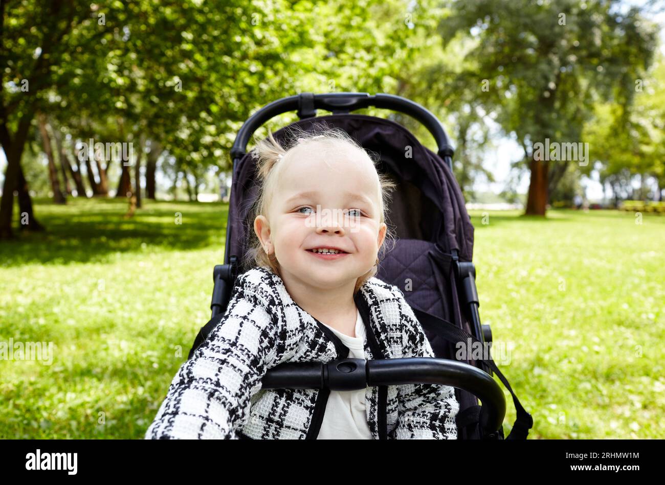 Bébé en poussette sur une promenade dans le parc d'été. Adorable petite fille assise dans une poussette et sourit. Enfant en buggy Banque D'Images