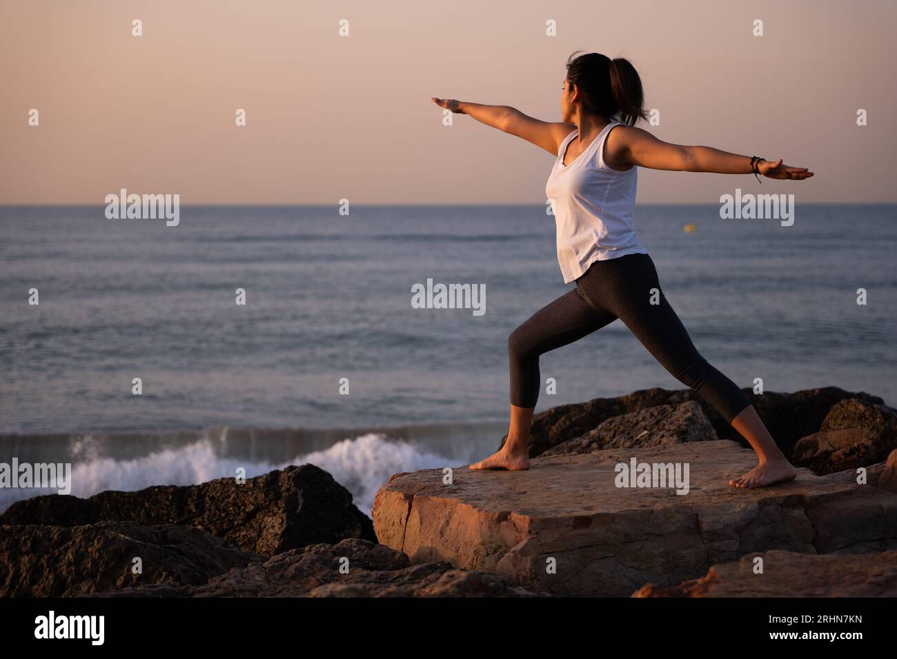 Femme faisant du yoga sur la plage avec la lumière du soleil illuminant son corps. Banque D'Images
