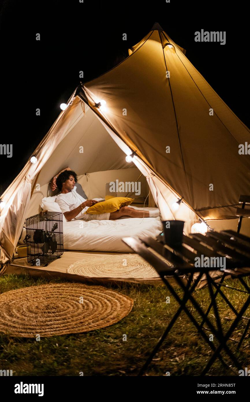 homme latin regardant une série sur l'ordinateur allongé sur le lit dans une tente Banque D'Images