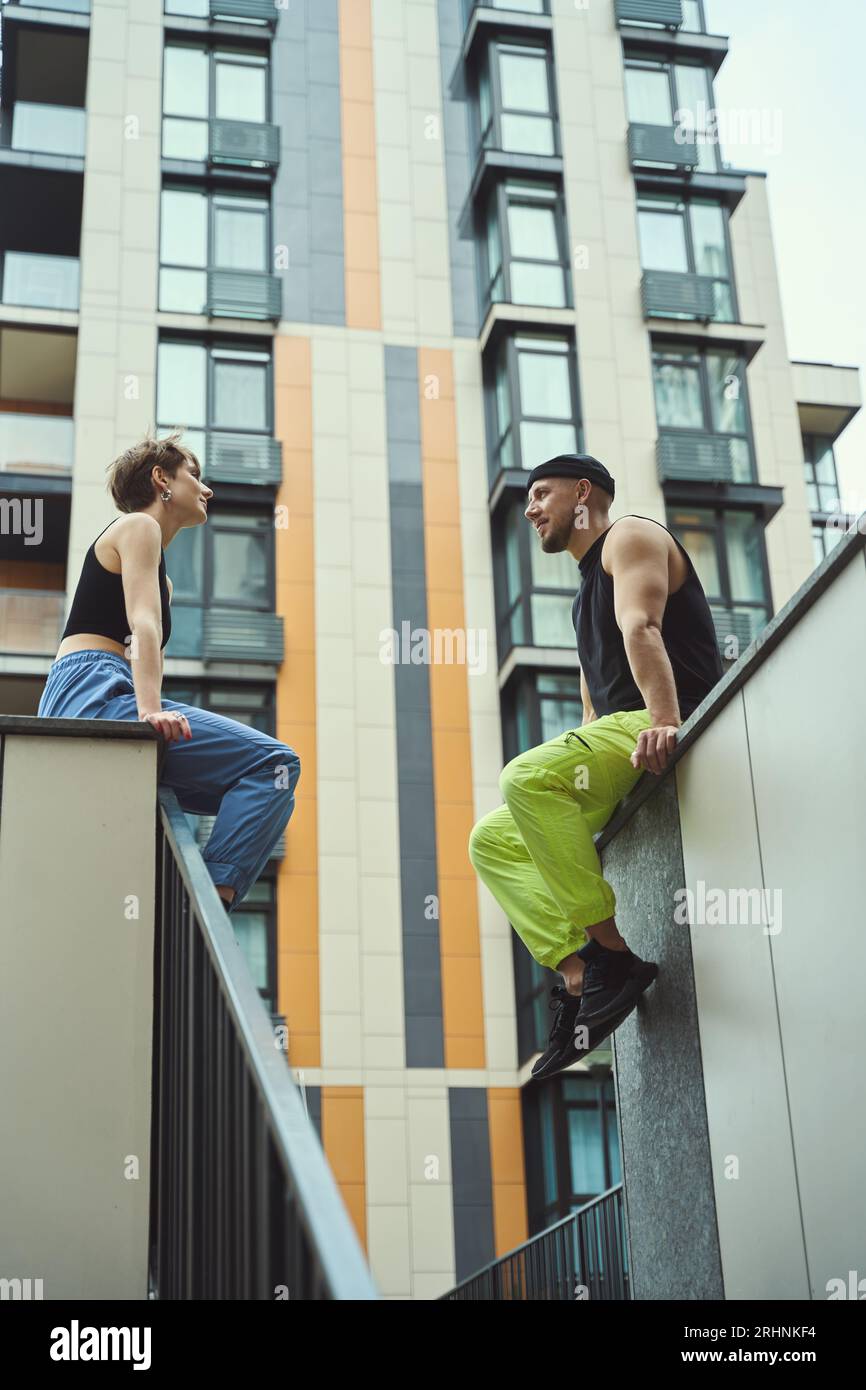 Le jeune homme et sa petite amie reposent sur un haut trottoir en face l'un de l'autre, à côté de grands bâtiments modernes Banque D'Images