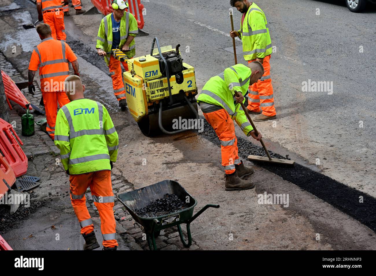 Ouvriers posant de l'asphalte et compactant avec rouleau vibrant finissant la tranchée dans la route pour conduit de fibre optique dans la mise à niveau des communications, Royaume-Uni Banque D'Images
