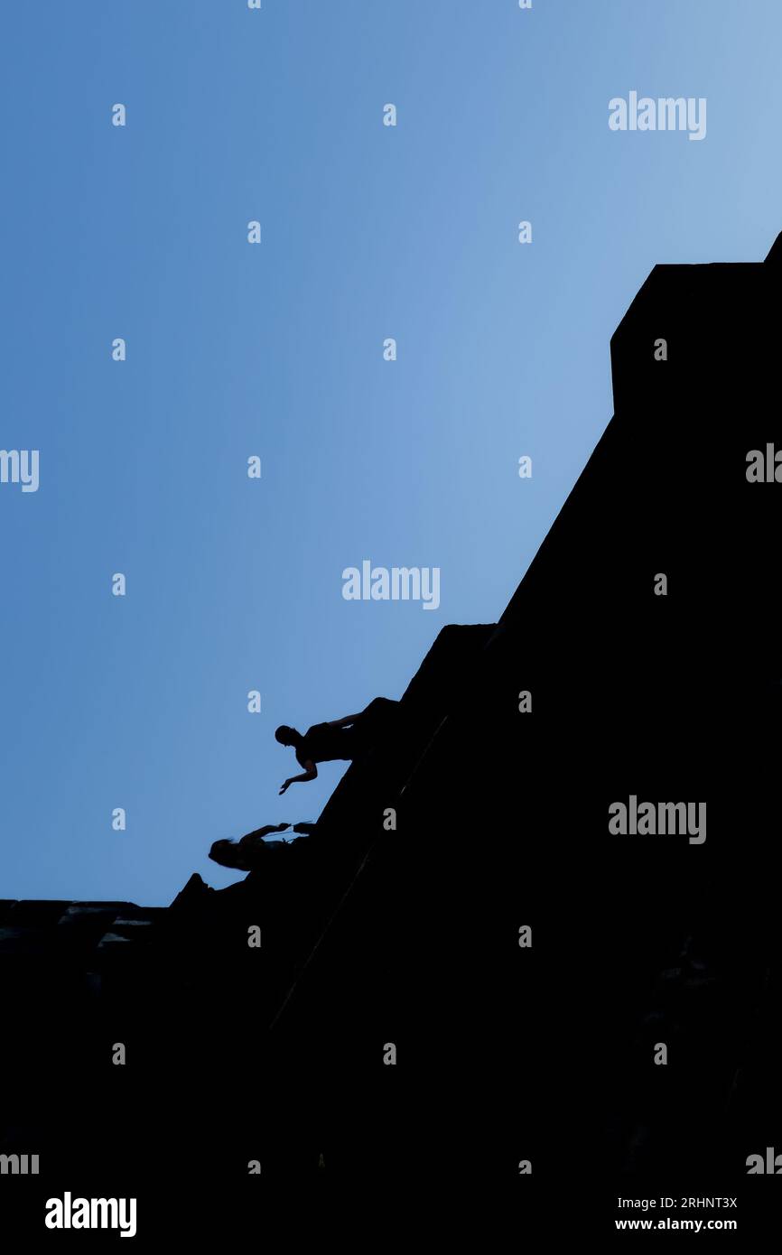 Silhouette de deux personnes assises au sommet d'un bâtiment en noir avec un ciel bleu clair en arrière-plan. La ligne entre le noir et le bleu court diago Banque D'Images