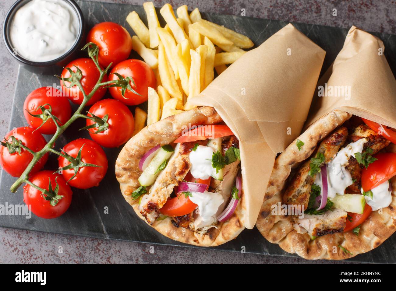 Gyros grecs de restauration rapide avec poulet, tomates, concombres et oignons servis avec sauce tzatziki et frites en gros plan sur une planche sur la table. Horiz Banque D'Images
