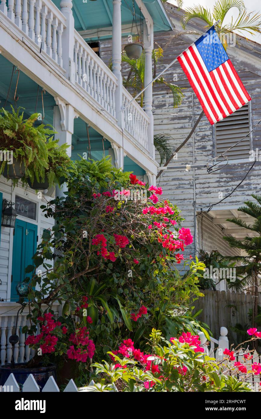 Key West, Floride, États-Unis. Balcon de maison typique en bois arborant le drapeau américain, bougainvilliers en premier plan, vieille ville. Banque D'Images