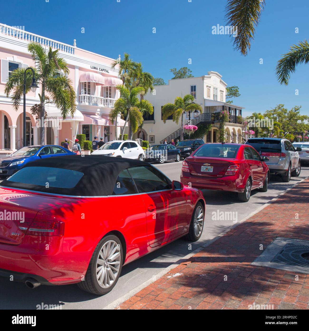 Naples, Floride, États-Unis. Voitures colorées garées dans la 3rd Street South bordée de palmiers, l'une des rues commerçantes les plus exclusives de la ville. Banque D'Images