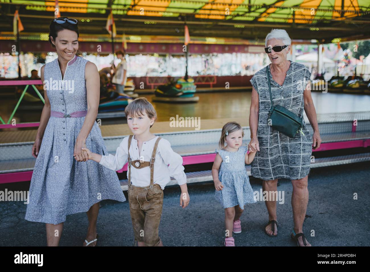 Frère et sœur marchent main dans la main avec mère et grand-mère à travers un champ de foire Banque D'Images