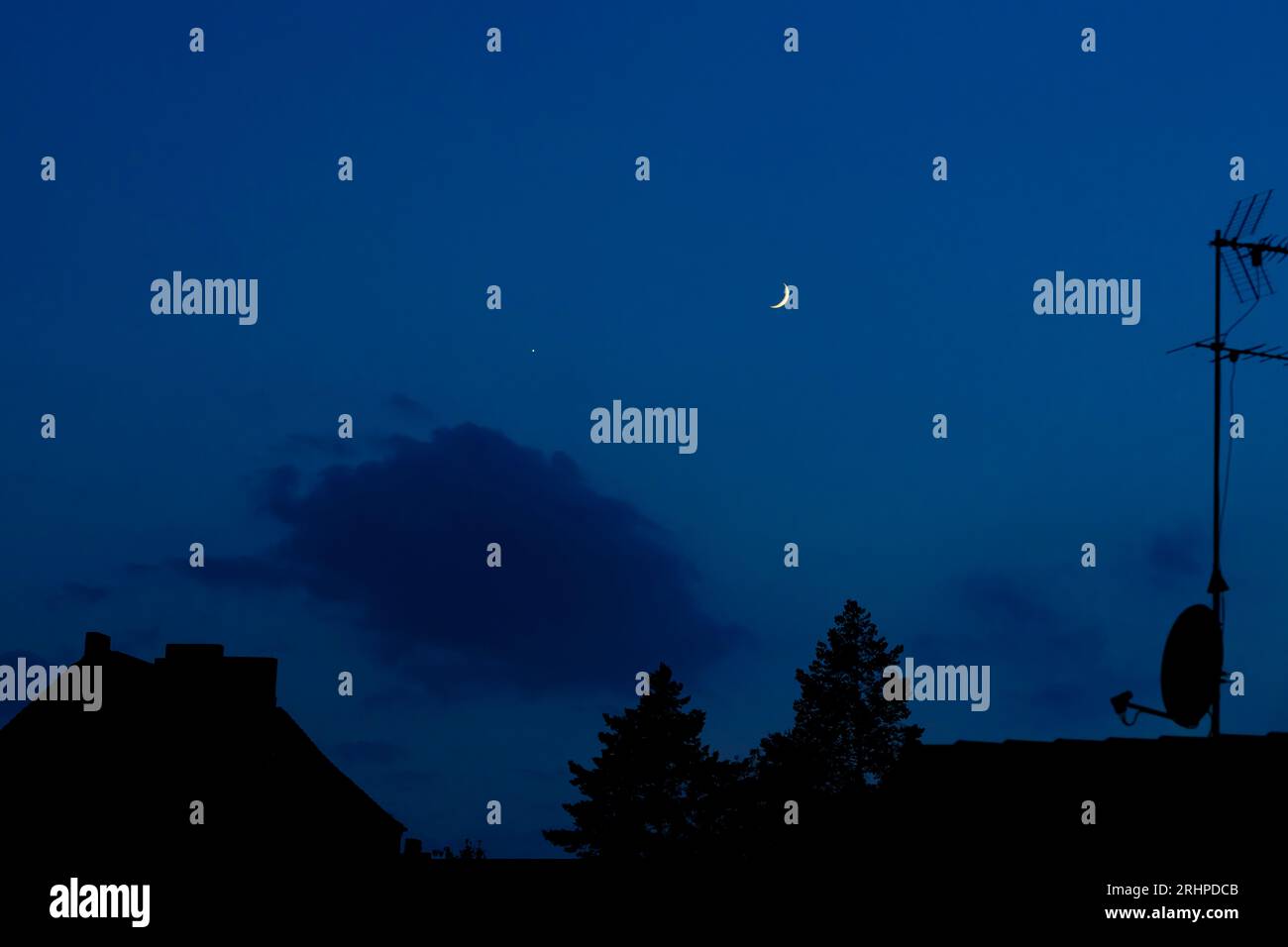Lune croissante le soir dans le ciel bleu au-dessus des toits de la ville Banque D'Images