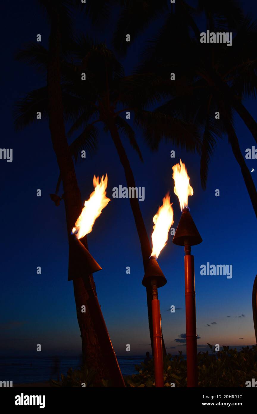 Les torches Tiki s'allument au crépuscule le long de Waikiki Beach Banque D'Images