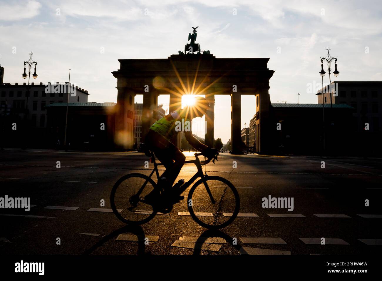 Berlin, Allemagne. 19 août 2023. Un cycliste passe devant la porte de Brandebourg alors que le soleil se lève. Les gens à Berlin et Brandebourg doivent se préparer à une chaleur forte à extrême samedi. Crédit : Christoph Soeder/dpa/Alamy Live News Banque D'Images