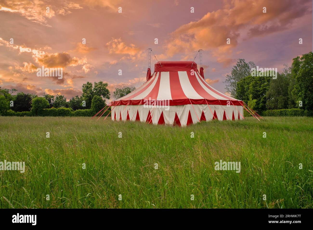 Tente de cirque colorée sur un pré vert contre un ciel de coucher de soleil coloré Banque D'Images
