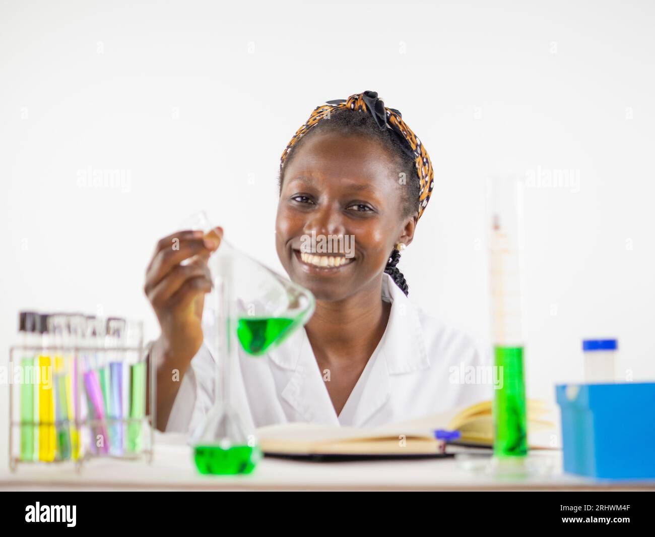Une jeune scientifique observe vivement un échantillon dans un flacon erlenmeyer à l'intérieur d'un laboratoire regardant la caméra Banque D'Images