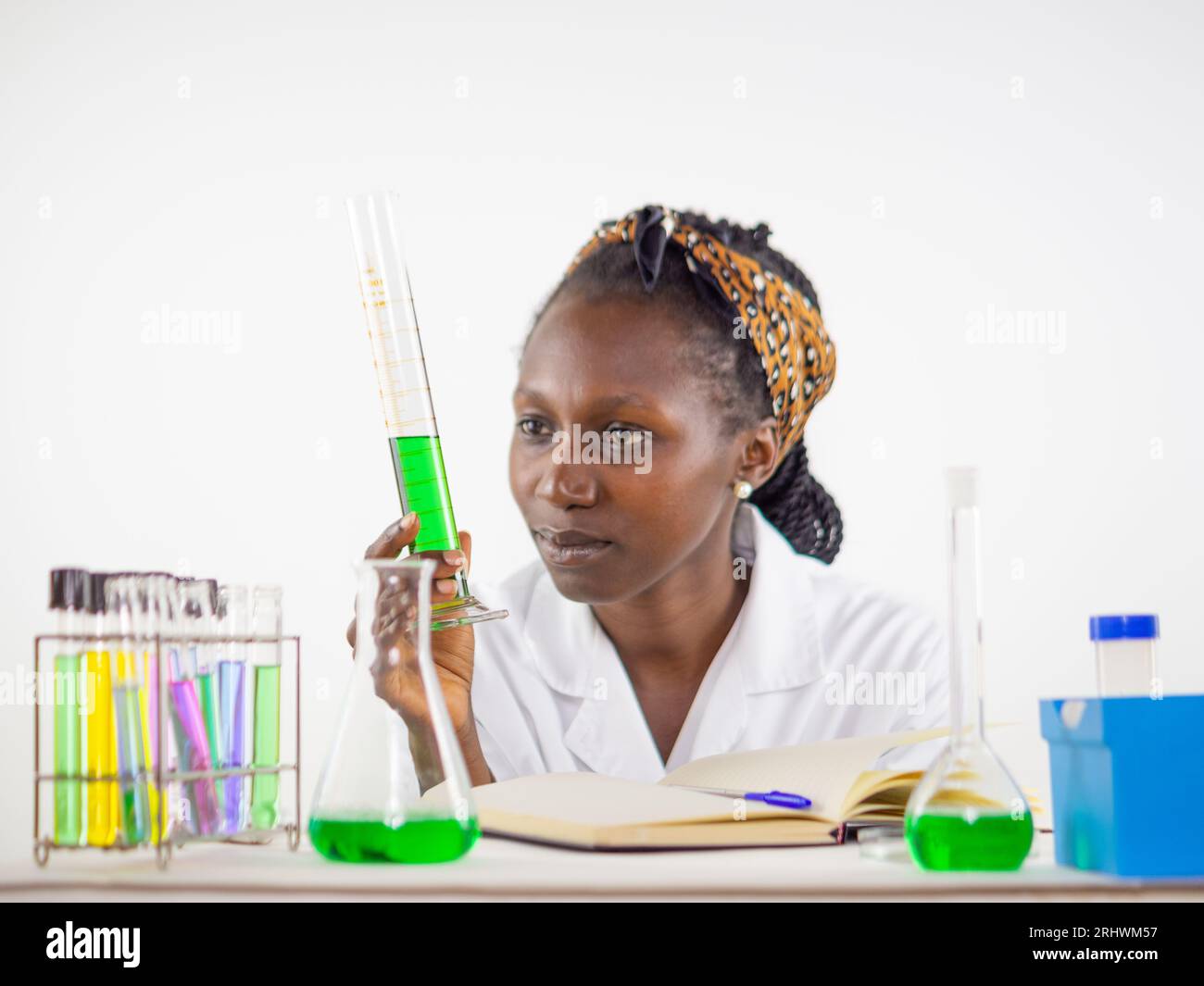 Jeune femme scientifique observant vivement un échantillon liquide tenu cylindre de mesure alors qu'il se trouvait dans un laboratoire Banque D'Images