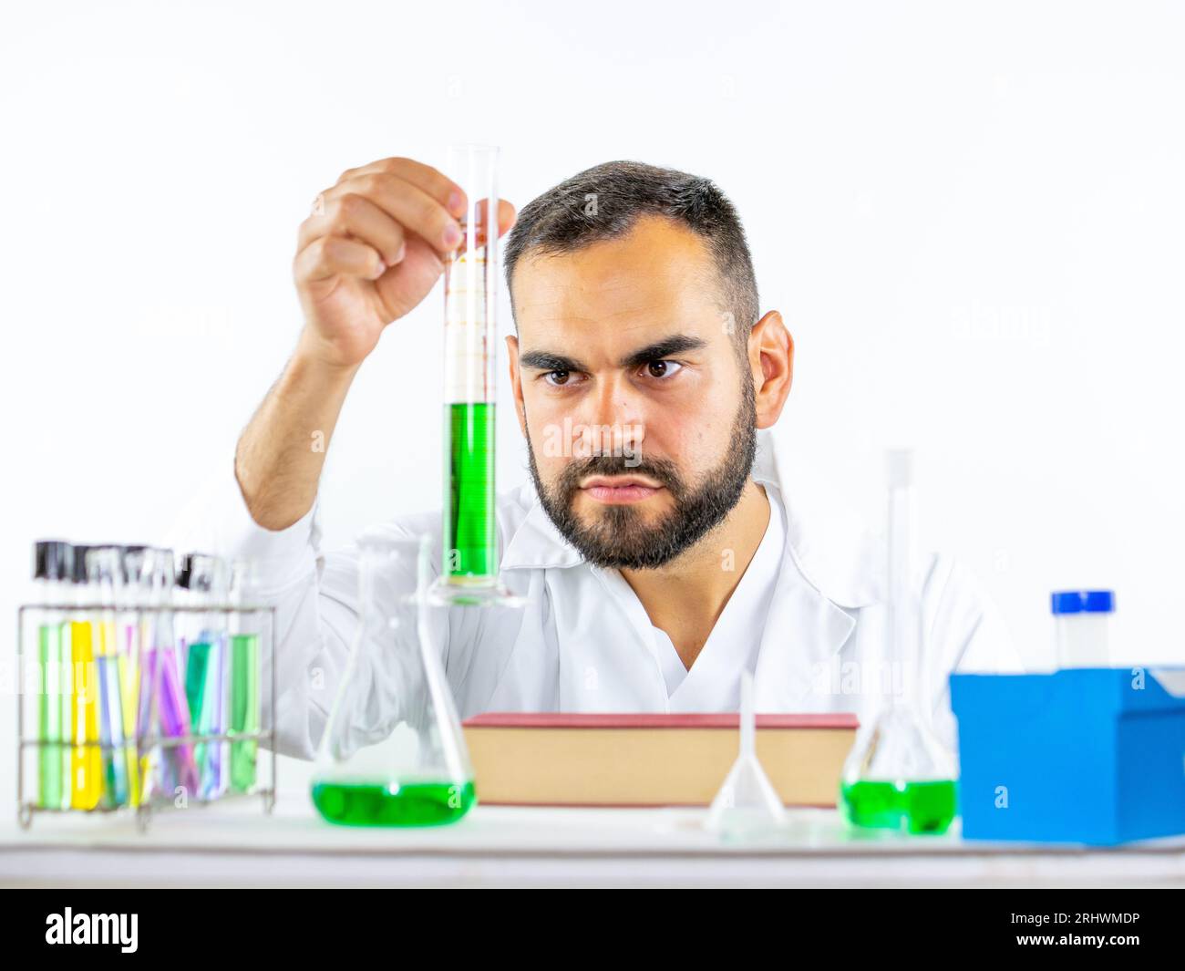 Jeune homme scientifique observant vivement un échantillon liquide tenu cylindre de mesure pendant qu'il se trouvait dans un laboratoire Banque D'Images