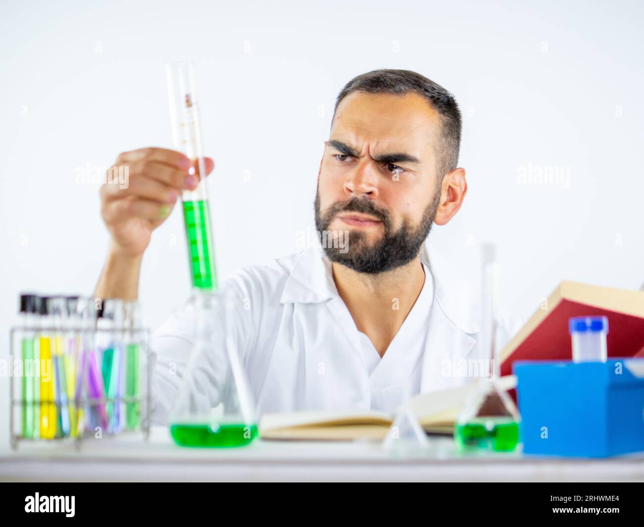 Jeune homme scientifique observant vivement un échantillon liquide tenu cylindre de mesure pendant qu'il se trouvait dans un laboratoire Banque D'Images