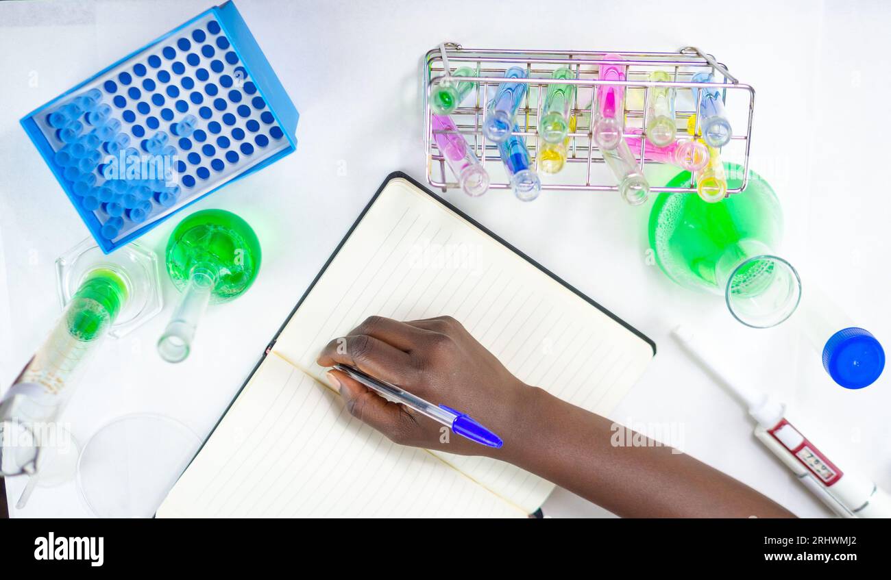 Gros plan de jeunes mains féminines écrivant sur un cahier dans un laboratoire avec un équipement de laboratoire Banque D'Images