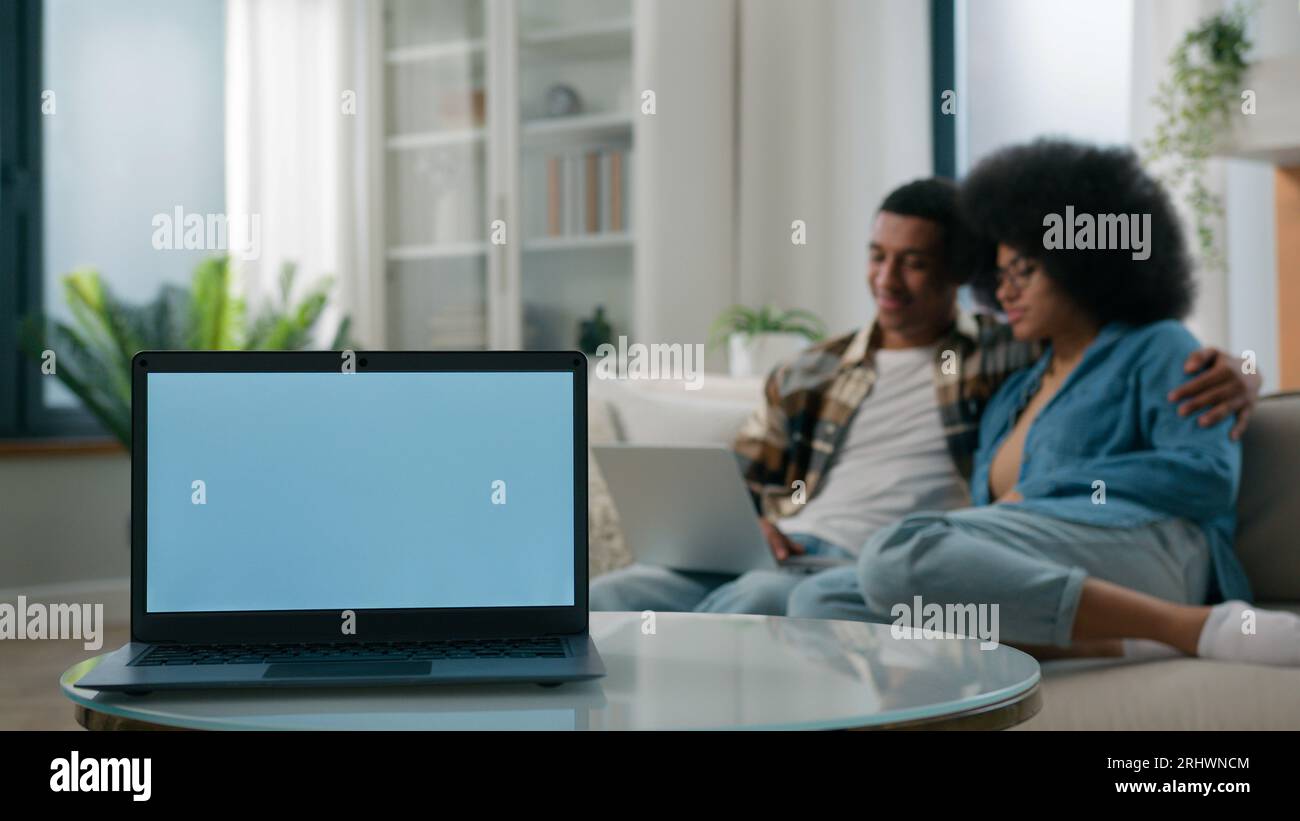 Ordinateur portable avec espace de copie vide gris écran bleu annoncez le modèle d'annonces sur le premier plan africain américain couple homme femme ensemble à la navigation de canapé à la maison Banque D'Images