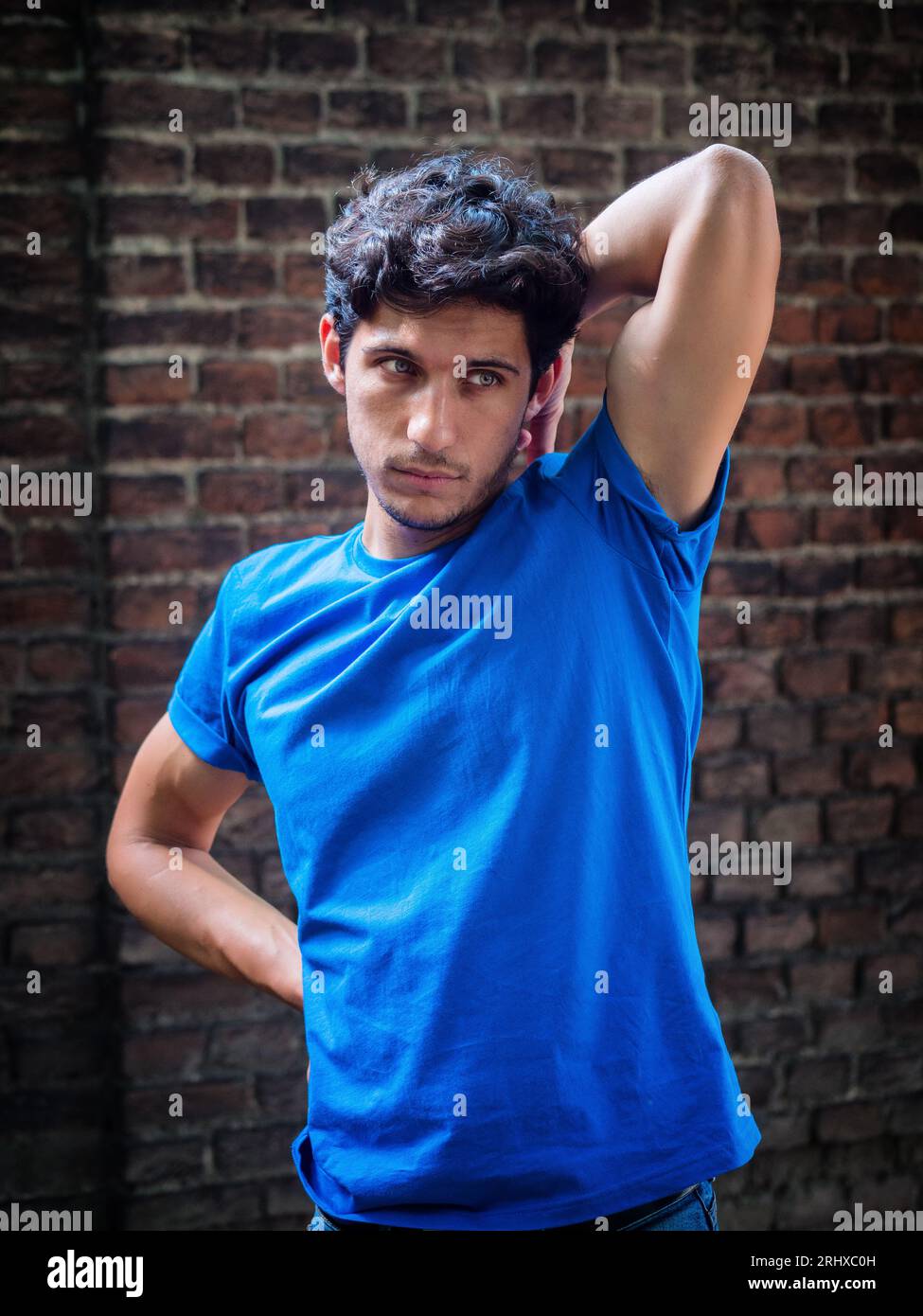 Photo de trois quarts d'un beau jeune homme en milieu urbain portant un polo bleu devant un mur de briques Banque D'Images