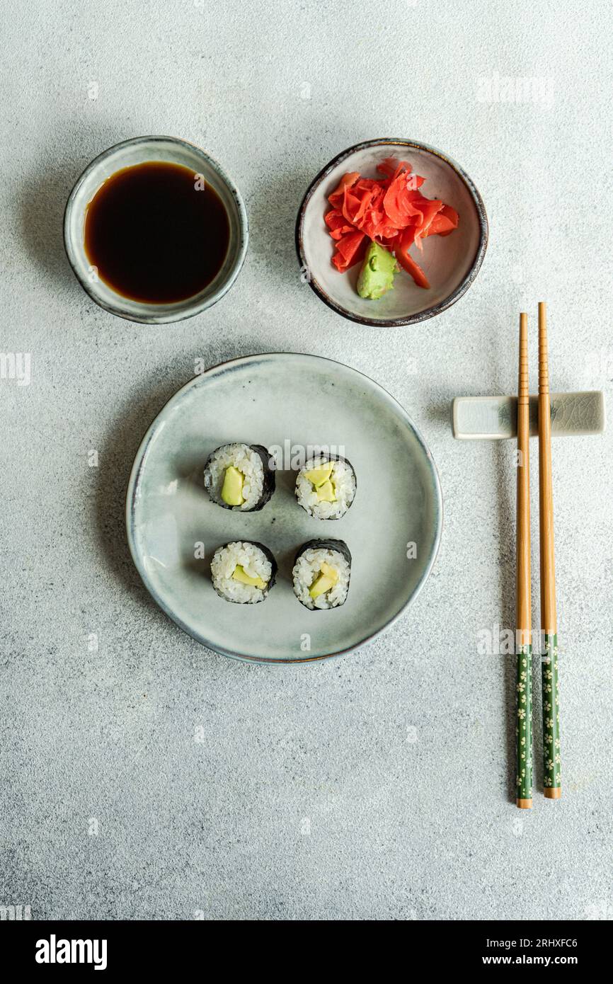 D'en haut de la nourriture japonaise ensemble avec un rouleau de maki avocat et sushi frit avec sauce soja et gingembre placé sur une table en béton blanc Banque D'Images